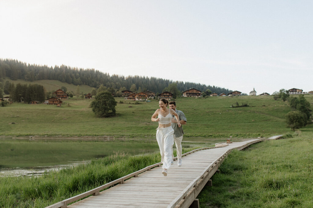 Un couple se courant après sur la passerelle du lac des confins sur la commune de La Clusaz. Ils rient et rayonnent de bonheur.